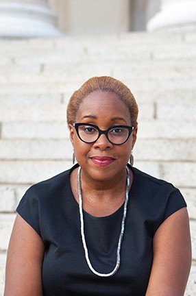 A woman wearing eyeglasses, a necklace, and a dark top.