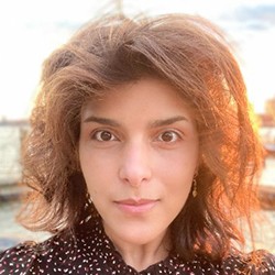 Headshot of Mariam Aly, a person with light brown hair, in a shot full of sunlight.