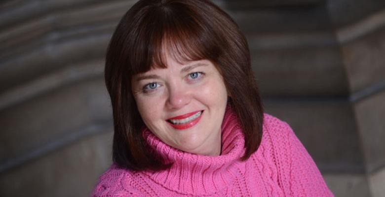 Mary Dooley smiles into camera as she is dressed in a pink sweater