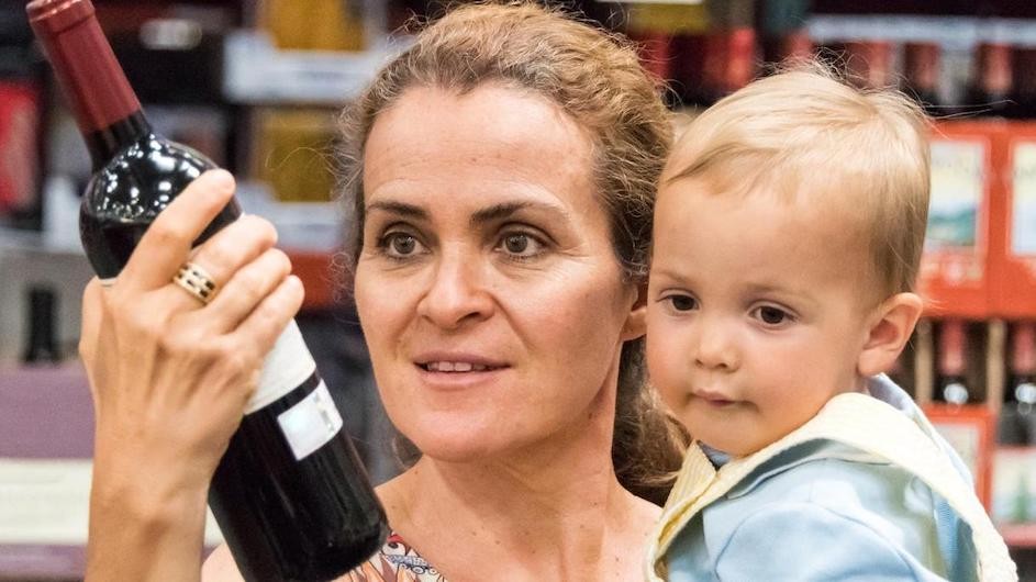 A mother holding a baby and a bottle of wine.