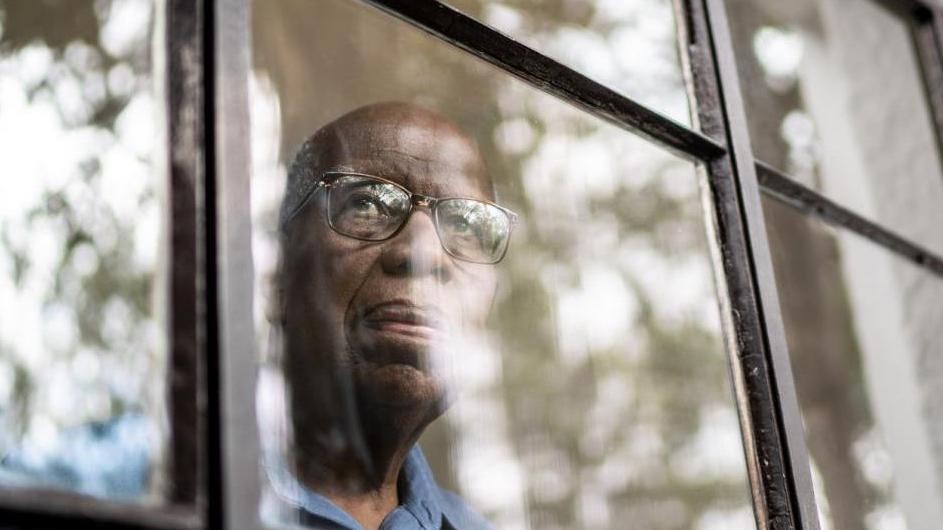 An older person looks out a window.