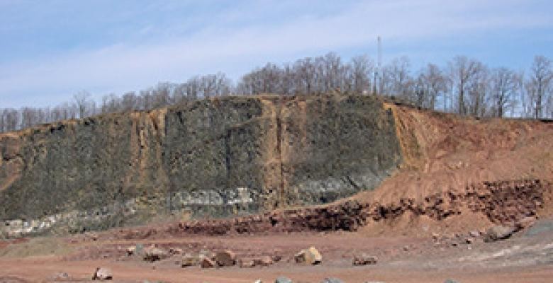 In suburban Clifton, New Jersey, a massive basalt flow (black rock, left) from the time of the End Triassic Extinction lies exposed in a former rock quarry, now behind a retirement home. A thin layer of sedimentary rock mostly covered in debris, at far right, records the sudden disappearance of many creatures. CLICK TO SEE VIDEO OF DRILLING IN NEW JERSEY. (Paul Olsen/Lamont-Doherty Earth Observatory)