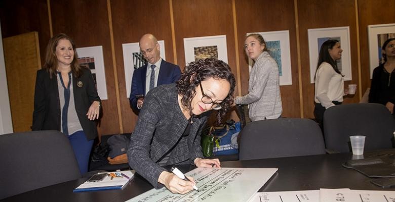 Young lady signs off on a document while supporters are standing around her