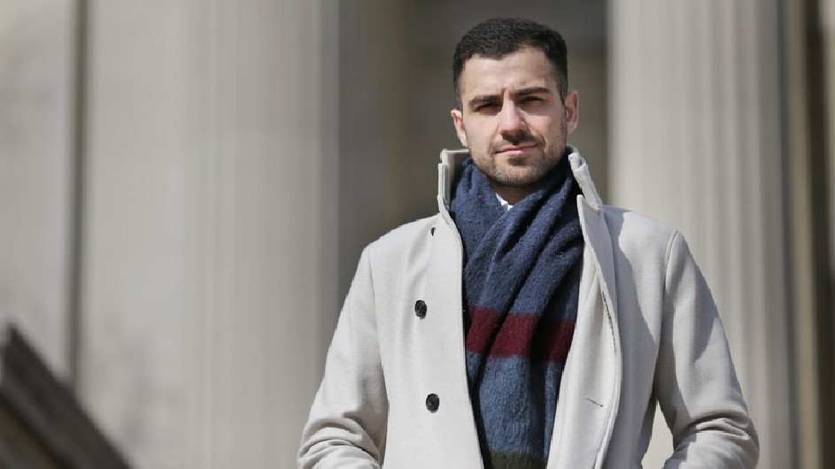 A man wearing a scarf is standing in front of columns.