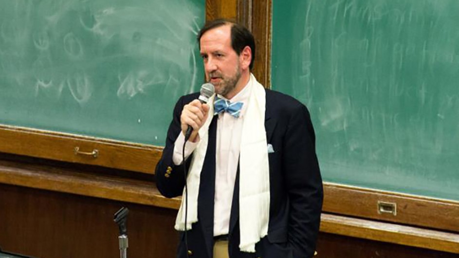 Thomas Vinciguerra has edited a new volume of essays about Columbia University Seminars. A man wearing a dark jacket and a white scarf holds a microphone and speaks in front of green chalkboards.