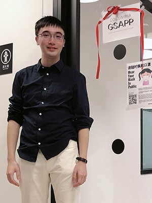 Ziming Wang: a man in a dark shirt and white pants stands before a door.