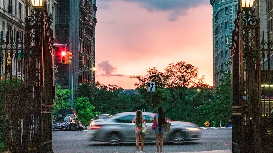 The sun sets over Columbia University's Morningside campus as two students get to the end of College Walk.