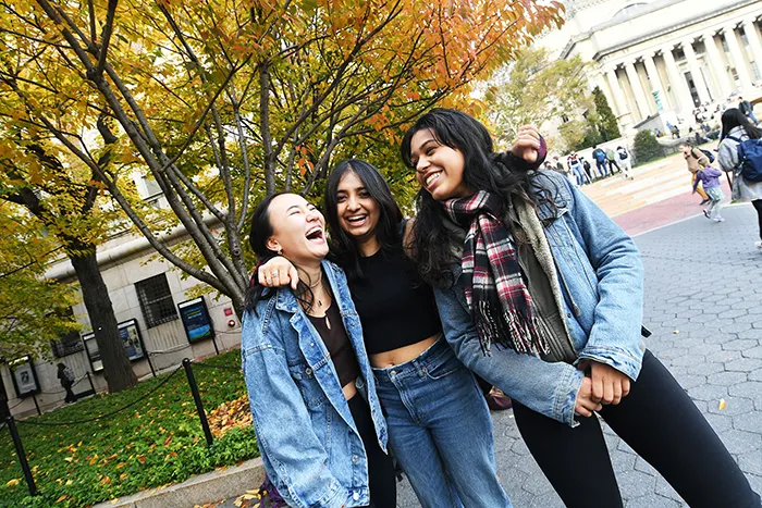 Three friends stand by fall foliage. 