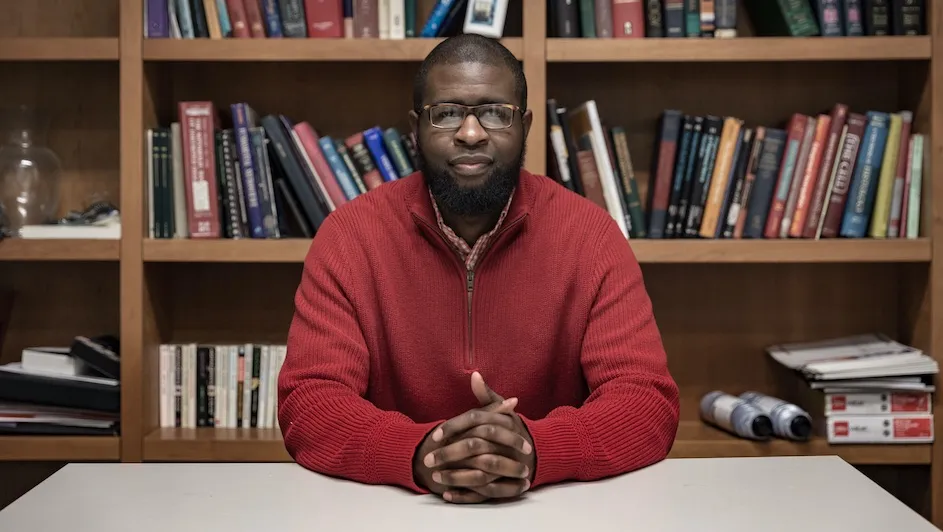 Ishmail Abdus-Saboor, an assistant professor in the Department of Biological Sciences in the Zuckerman Mind Brain Behavior Institute, has been selected to join the Pew Scholars Program in the Biomedical Sciences. Here he sits at a desk with bookshelves in the background.