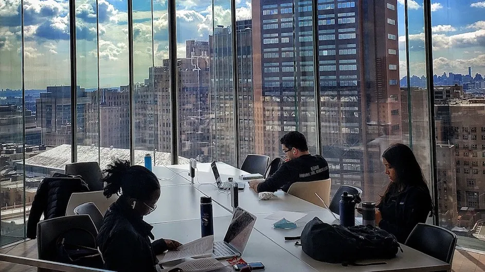Medical school students studying in a room with large windows on a high floor overlooking buildings