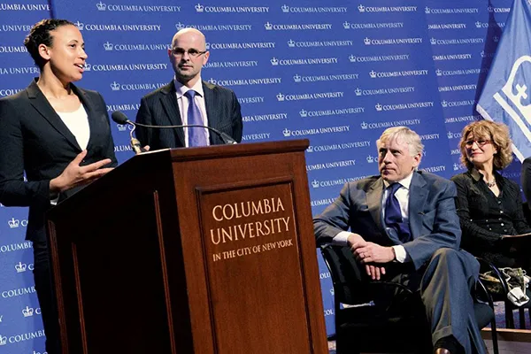 Two people stand at a lectern to receive the Global Freedom of Expression Prize at Columbia, as an assembled group looks on. 