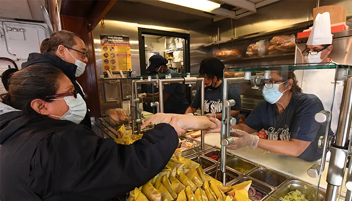 Two people wait in line for subs. 