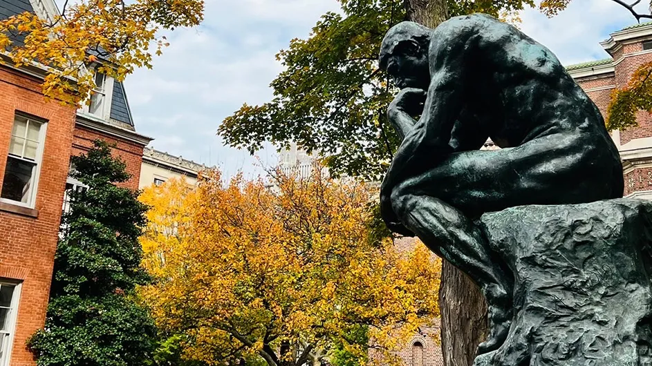 Vibrant yellow and orange leaves overhang from trees above the statue of "The Thinker" on Columbia's Morningside campus.