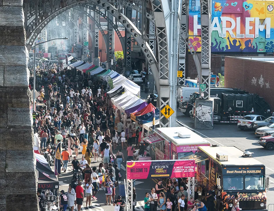 Uptown Night Market festival with people enjoying food and music under the arches of the aqueduct near Columbia Manhattanville