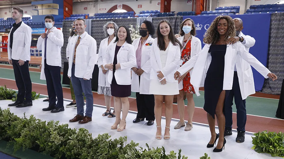 Six Columbia medical students in white coats stand in front of six faculty members in white coats at Columbia's Vagelos College of Physicians and Surgeons' White Coat Ceremony.