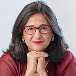 Minouche Shafik, a woman with long dark hair, in red glasses and a red top. 
