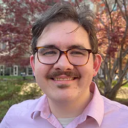 A man with short, dark hair, glasses, and a mustache. 