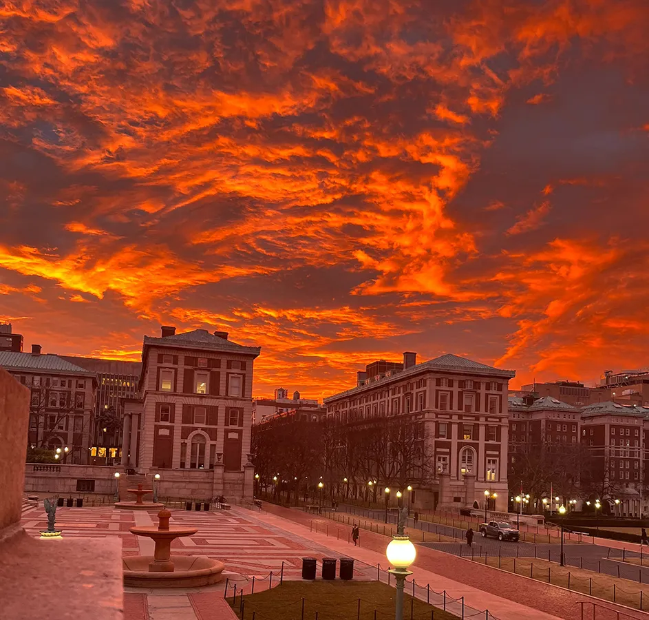 Low Plaza, Kent Hall, and Hamilton Hall against a cloudy orange sky during sunrise at Columbia University.
