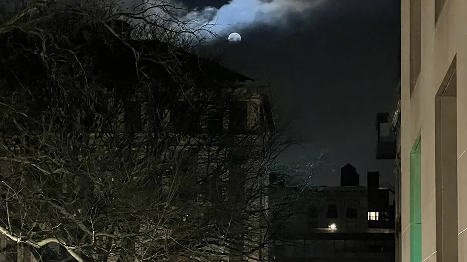 The bright full moon glows above Columbia University's Havemeyer and Math Plaza near Scholars' Lion statue with a view of Barnard College's illuminated library in the distance.
