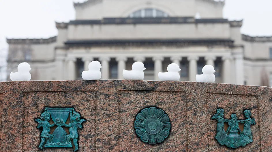 Five snow duck peeps on the Sundial sculpture with Low Library in the background on a cloudy winter day at Columbia University.