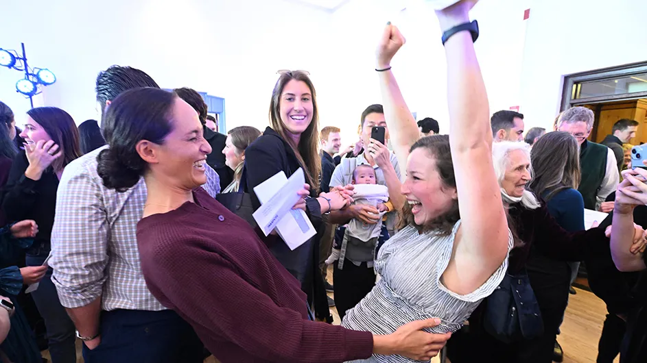 Two medical students holding opened letters and envelopes smile and embrace each other as they learn where they have matched for their medical residency as family, friends, and other students smile and celebrate all the graduating medical students at Columbia University Irving Medical Center.