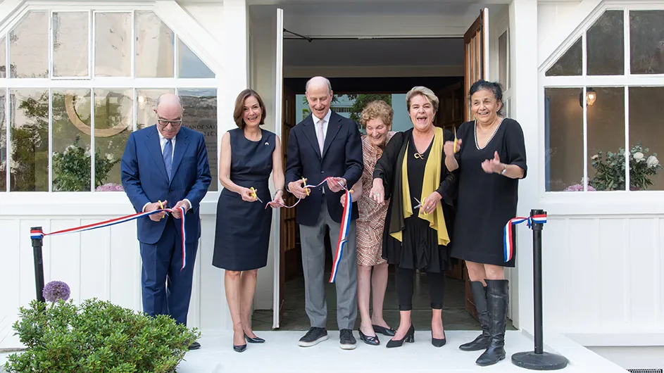 Six people pose and smile as they cut the ceremonial ribbon to an opening of a great hall at the Columbia Global Center in Paris.