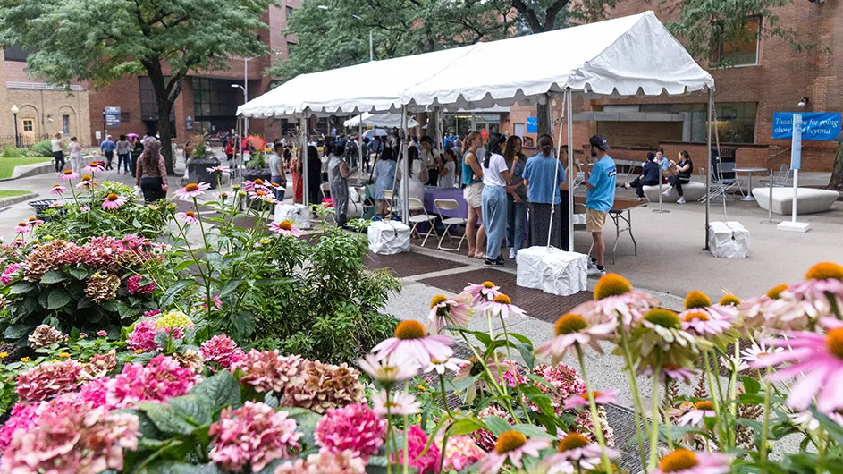 Dozens of Columbia Med employees and neighbors gather on summer-flowered-lined Haven Plaza under and near a big white tent for an ice cream social on an overcast day at Columbia University Irving Medical Center.