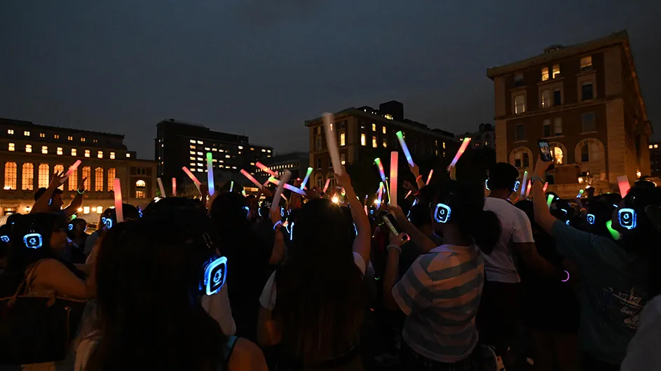 Dozens of students dance while wearing headphones at a silent disco at night on Low Plaza at Columbia University.