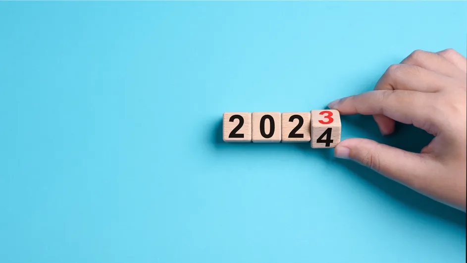 A hand turns over wooden blocks from 2023 to 2024. 