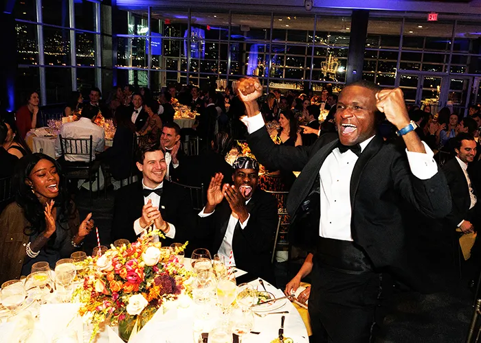 A student veteran in a tuxedo stands up to cheer from his table during the 2024 Military Ball.