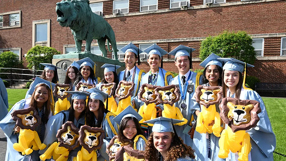 Columbia College grads pose in front of the Baker Field Lion.