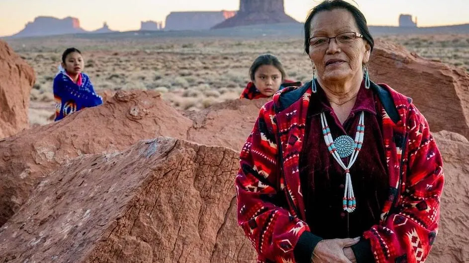 Photograph of an older woman looking at the camera, with two children in the background.