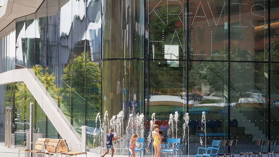 Four children play and splash in the water sprinkler in front of Kravis Hall at Columbia Manhattanville's campus on a hot sunny day.