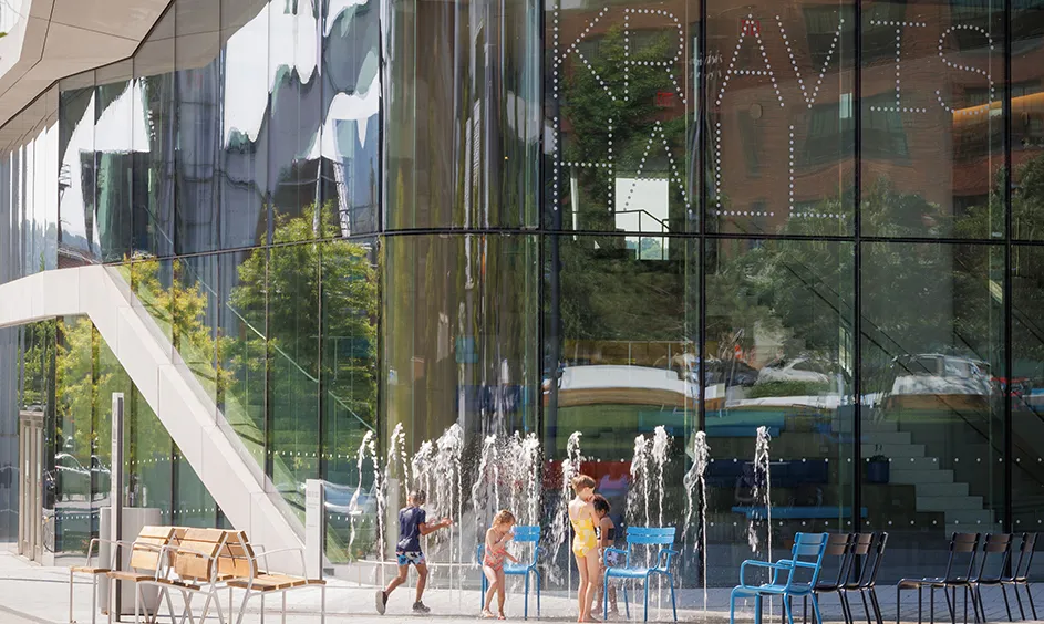 Four children play and splash in the water sprinkler in front of Kravis Hall at Columbia Manhattanville's campus on a hot sunny day. 
