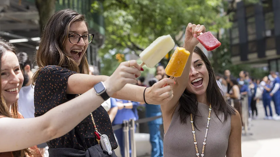 Three women smile and hold up popsicles at Columbia University Irving Medical Center's Ice Cream Social on a hot summer day. 