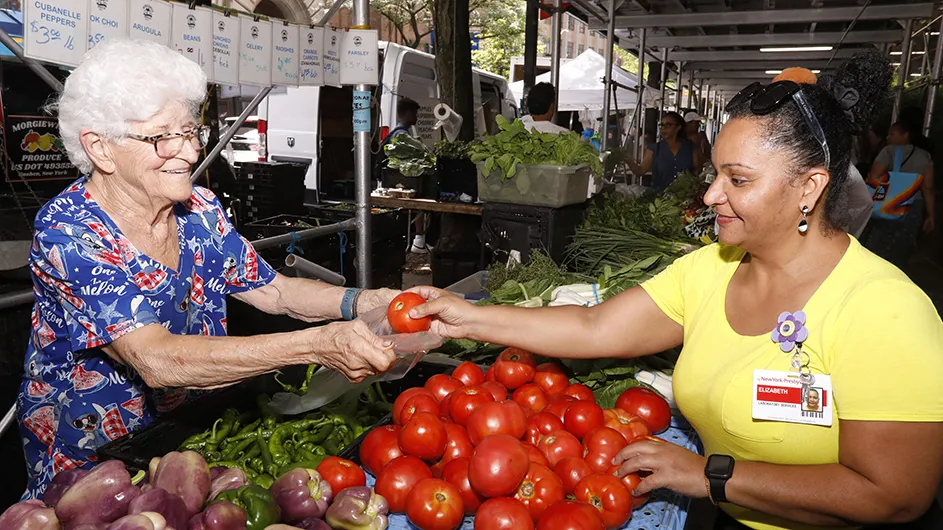 A woman smiles and puts a red tomato in a bag held by a produce vendor at the Farmers' Market at Columbia Medical Center. 