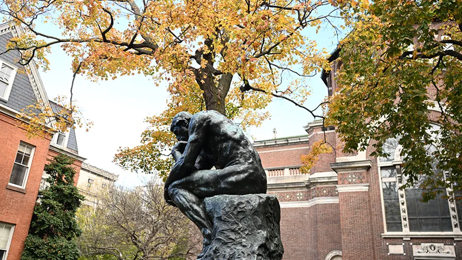 The Thinker statue on Columbia's Morningside campus under a cover of fall leaves.