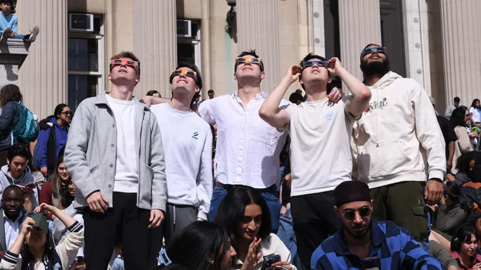 Five students in white shirts look up at the solar eclipse. 
