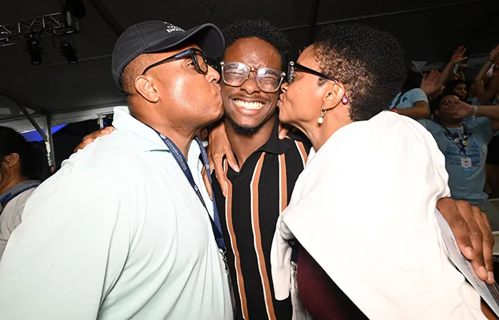 A student is kissed by their Mom and Dad on the cheek.