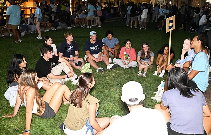 A group of students and their NSOP leader sit in a circle at night on the South Lawn.