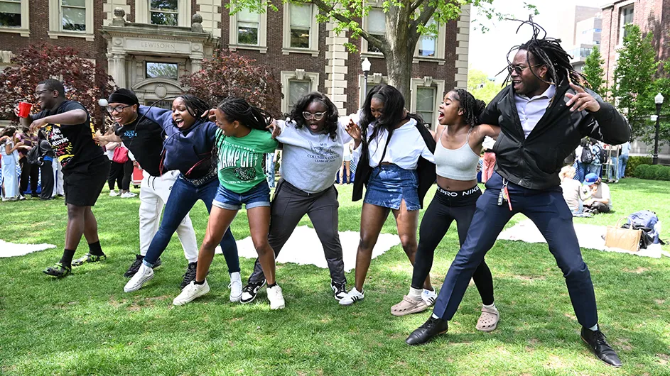 Students dancing in a line on the quad in front of Lewisohn Hall on Morningside campus. 