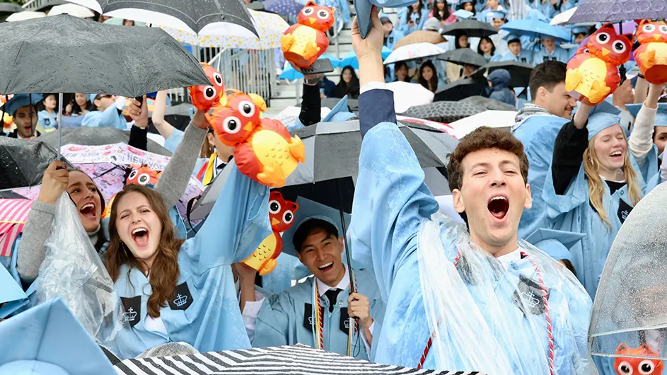 Graduates of Columbia's School of General Studies smile and jump for joy under umbrellas. 