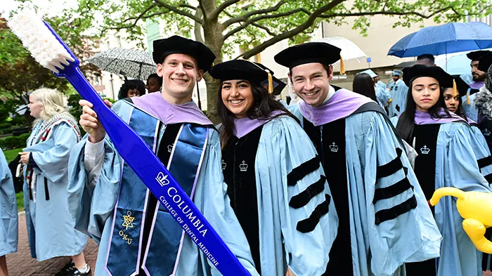 Three Columbia Dental School graduates hold a gigantic toothbrush on Morningside campus.