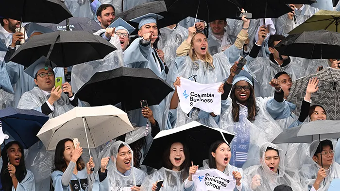 Columbia Business School grads wave flags under umbrellas during Commencement.