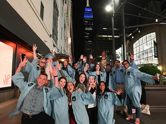 A group of friends in Columbia graduate gowns poses at 34th Street and 7th Avenue with the Empire State Building in the background.