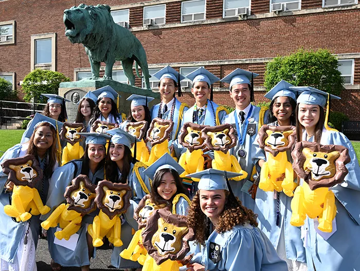 Several Columbia College grads smile and pose while holding inflatable balloon lions in front of the lion statue at Baker Athletics Complex. 
