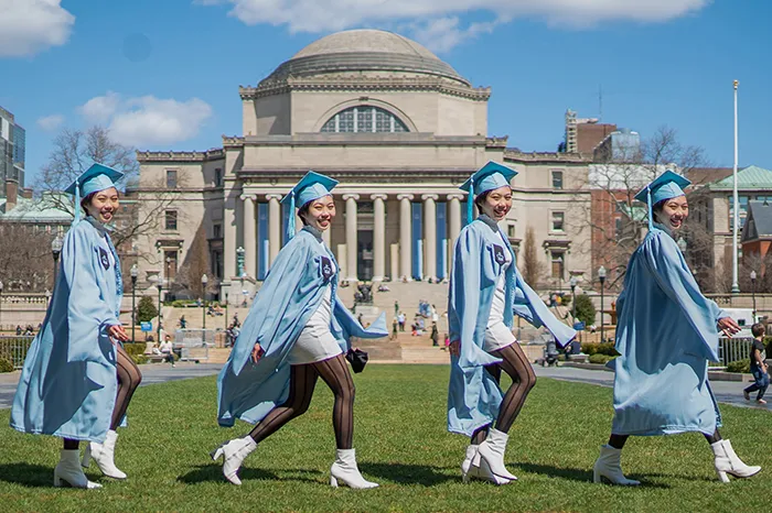 Rachel Yeung in cap and gown walks in front of Low Library