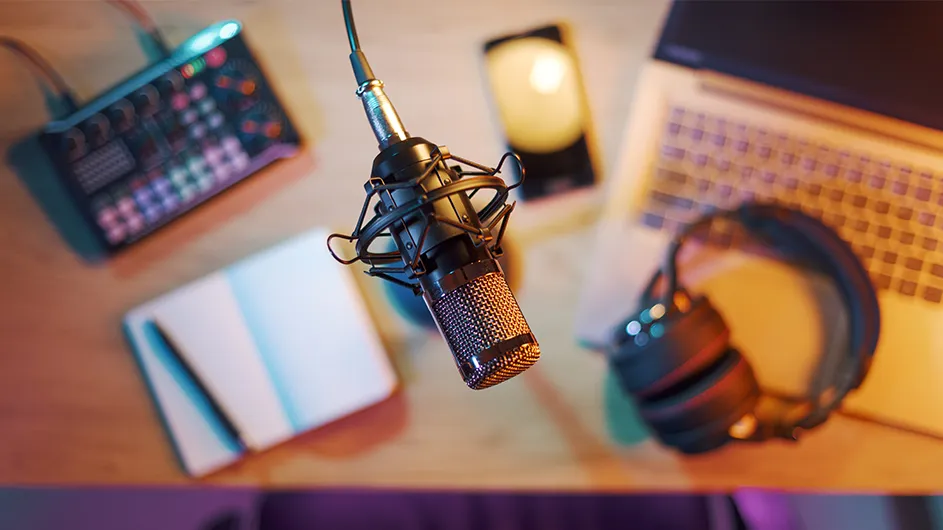 Podcast equipment like a laptop, microphone, headphones, and a mixing board. 