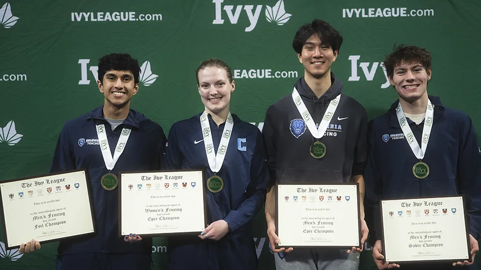 Four university fencing athletes in Columbia uniforms smile and pose for the camera wearing championship medals and holding up awards at the Ivy League Fencing Championships.