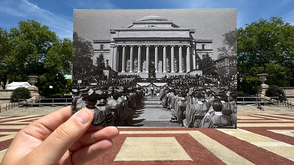 A hand holding up an archival 1987 photo of university graduates on Low Plaza with Low Library in the background on a sunny Commencement Day at Columbia University. 